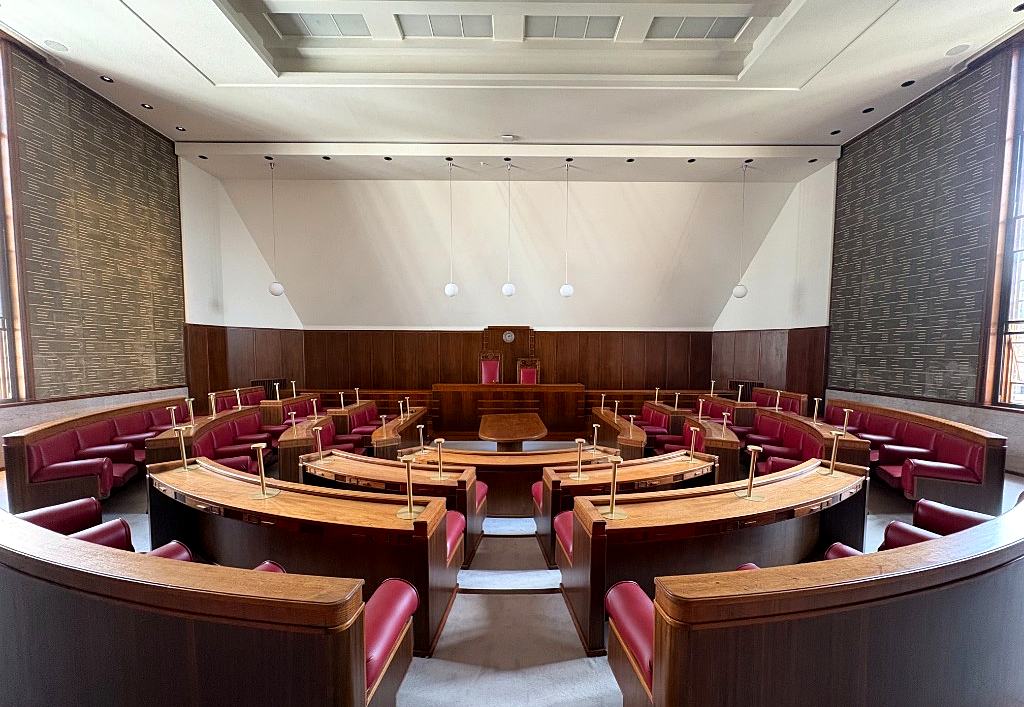 The Council Chamber seen from the entrance, with curved wooden desks and red seats